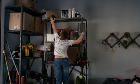A young boy reaches for an unsecured gun on a high shelf in a garage